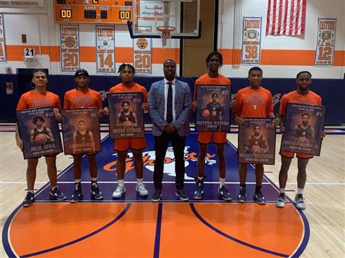 Seven people stand in the middle of an indoor basketball court posing for a photo.
